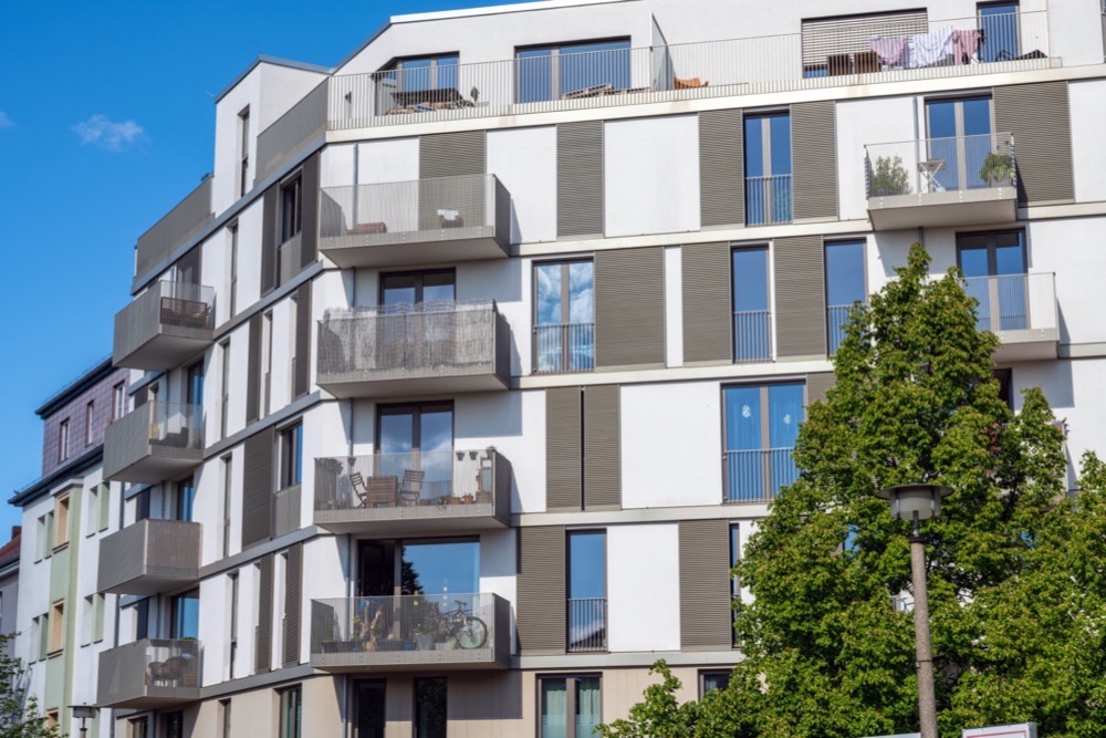 Mehrfamilienhaus mit umlaufenden Balkonen vor blauem Himmel